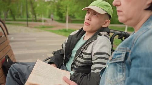 Teen Reads Book with Woman in Sunny Park