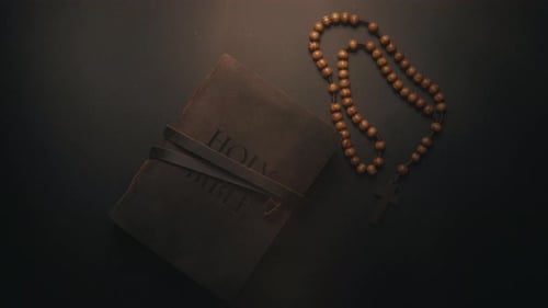 Holy Bible with Wooden Rosary on Dark Surface