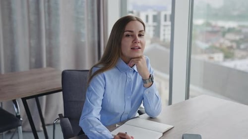 Young female employee sitting at desk in the office thinking over some issues.