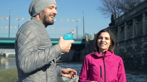 Sporty Couple Of Joggers Drinking Water In City