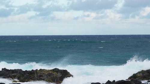 Ocean waves crashing against rocky coastline under cloudy sky