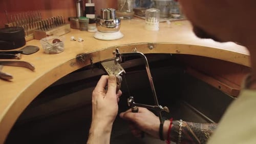 A Man is Working on a Piece of Jewelry Using a Tool to Cut a Piece of Metal