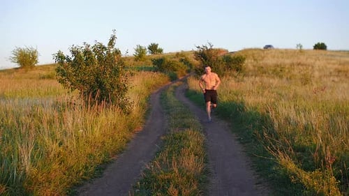 Muscular Shirtless Man Jogging Down the Hill at Sunset in Slow Motion