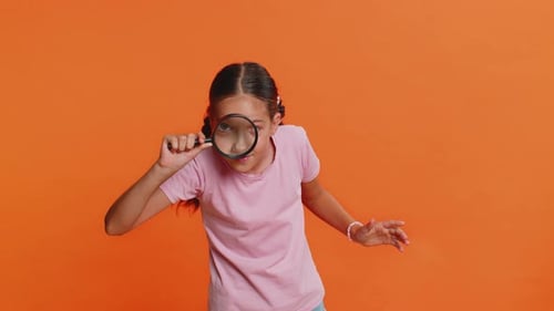 Une fillette tient une loupe près de son visage en regardant la caméra avec un grand œil zoomé pour analyser