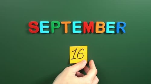 Hand sticking a sticker 16 September calendar day on school board. 16 date of September. Sixteenth