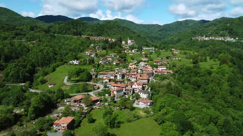 Beautiful aerial of Italian town on slopes of green forested hills, Piedmont, Italy