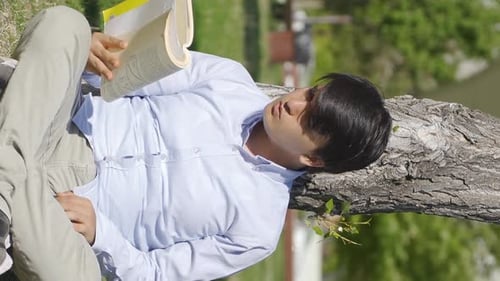 Vertical Video of Young man reading a book in the park.