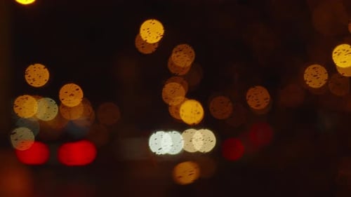 Water drops flow down the windshield at night view from car. Urban Night Lights Blur. Cityscape