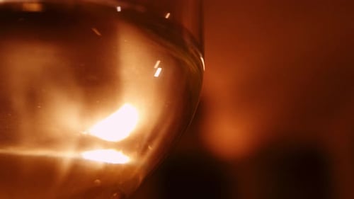 Close-up view of transparent white wine in glass held up against warm light