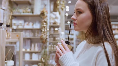 Young Lady Smelling Perfume Bottle in Mall with Blurred Background