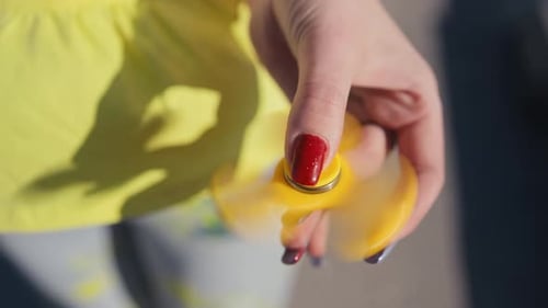 Un fidget spinner jaune qui tourne, tenu à la main tout en portant des vêtements colorés et tendances aux couleurs vives