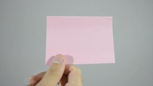 Hand Places Pink Sticky Note on Gray Background