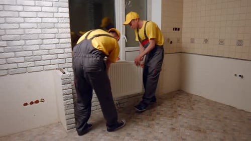 Arbeiter installieren eine Heizkörperheizung in der Küche und reparieren in einem neuen Gebäude