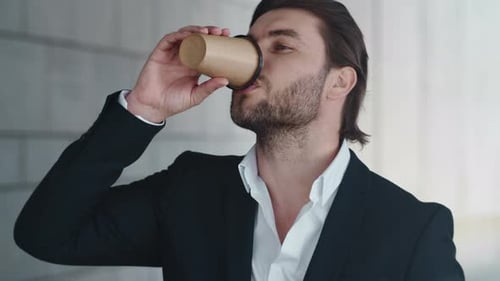 Serious businessman drinking coffee and checking time on wristwatch in city street