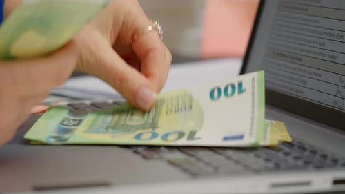 Macro shot of euros being laid on a laptop keyboard female in office.