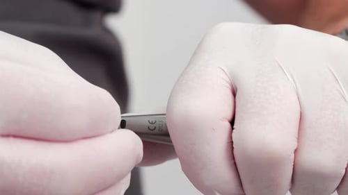 Nahaufnahme von Zahnarzthänden in weißen Handschuhen, die einen Zahnbohrer in das Handstück stecken, Vorbereitung für