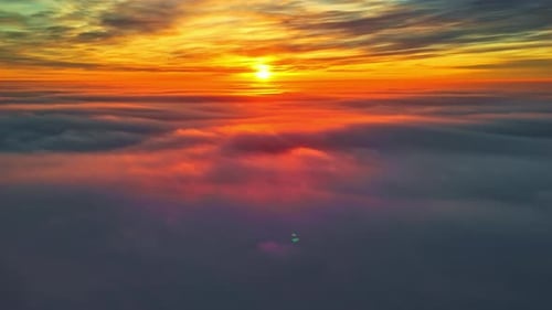 Vue aérienne au-dessus de nuages épais pendant un coucher de soleil éclatant, avec une lumière orange rougeoyante se répandant sur