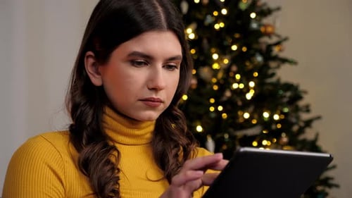 Mujer que usa tableta compra regalos de Año Nuevo en Internet sobre un árbol de Navidad de fondo