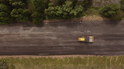 Aerial top down view of road roller, leveling sand and gravel during countryside road construction.