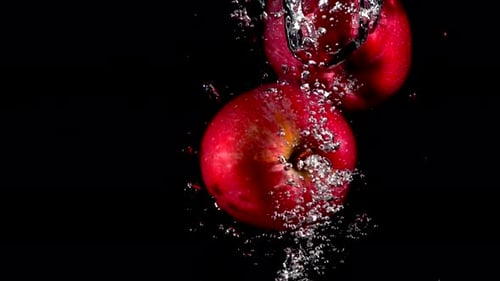 Slow Motion Red and Yellow Apple Falling in Water on Black Background
