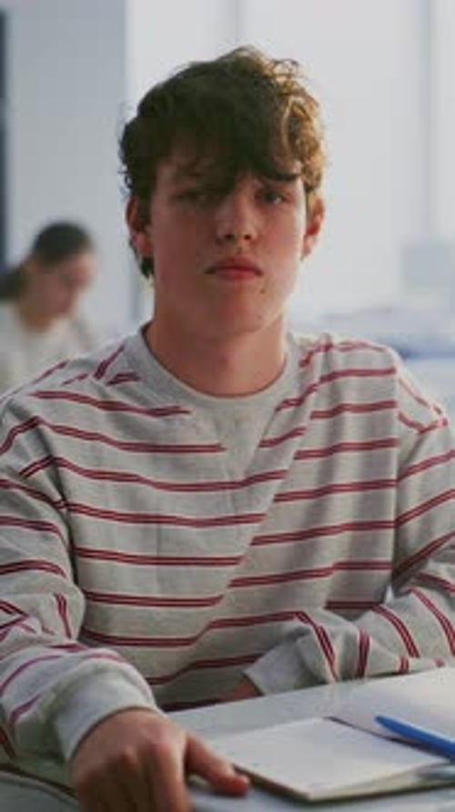 Young Student in Striped Sweatshirt With Focused Expression Sits Desk
