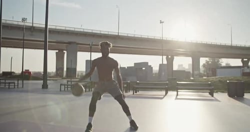 Man Dribbling Basketball on Urban Court in Sunlight