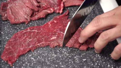 Person Slicing Raw Beef Steak on Cutting Board