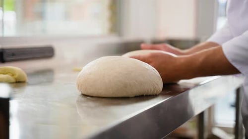 Hands Kneading Loaf of Dough on Metal Table