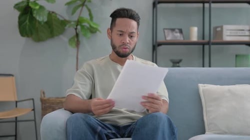 Man Looks Frustrated Reading Paperwork at Home