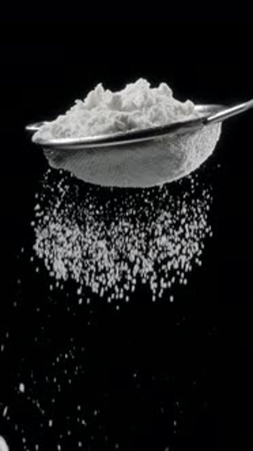 Sift icing sugar or powdered sugar or flour through a sieve tool on black background.
