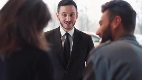Consultor de vendas atraente conversando com jovens: casal feliz comprando um vendedor de veículos com barba
