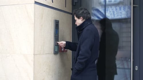 Young teenage boy enters modern apartment building using security intercom
