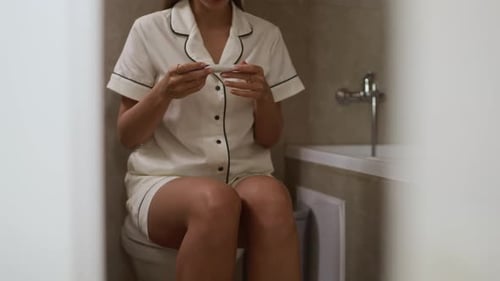 Woman in pajamas looking at pregnancy test in bathroom