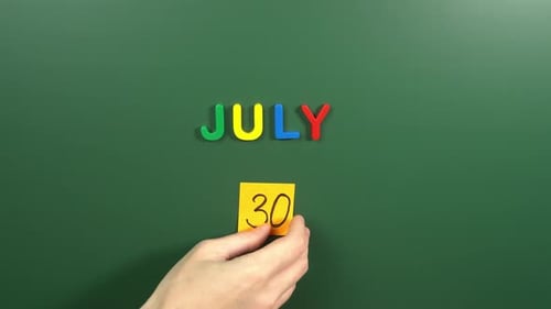 Hand sticking a sticker 30 July calendar day on school board. 30 date of July. Thirtieth day