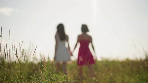 Two Women Holding Hands Walking Through a Field