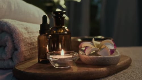 Close-up of Oil Bottles, Lit Candle and Frangipani Blossoms in Spa Salon
