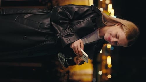 Vertical Video Smiling Girl Standing Outside at the Night Street Scrolling Social Media on Phone