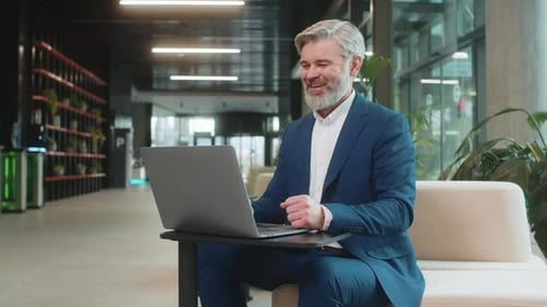 Confident Businessman Using Laptop Talking on Online Communication Video Call in Modern Office Lobby