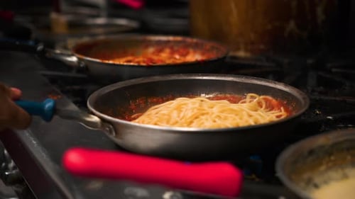 Chef stirs tosses and swirls fresh cooked pasta into steaming tomato sauce over italian restaurant p