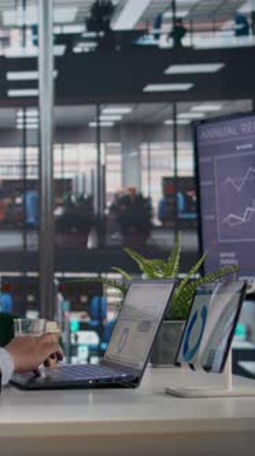 Professional at desk uses laptop, views financial charts