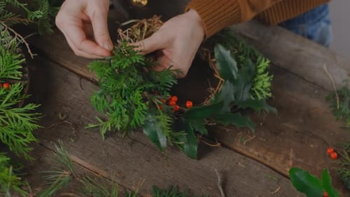 Hands Making Christmas Wreath on Wood Table