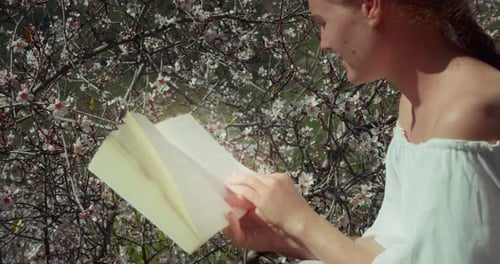 Girl reading a book outdoors. Close-up of woman face with open dairy in hands. Spring flowers blurre