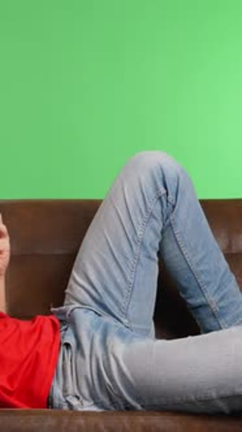 Man Relaxing on Sofa Using Smartphone with Green Screen