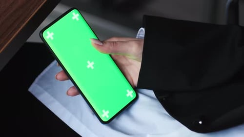 View of Female Hand Holding and Pressing on Smartphone with Mockup Green Screen Indoor Office