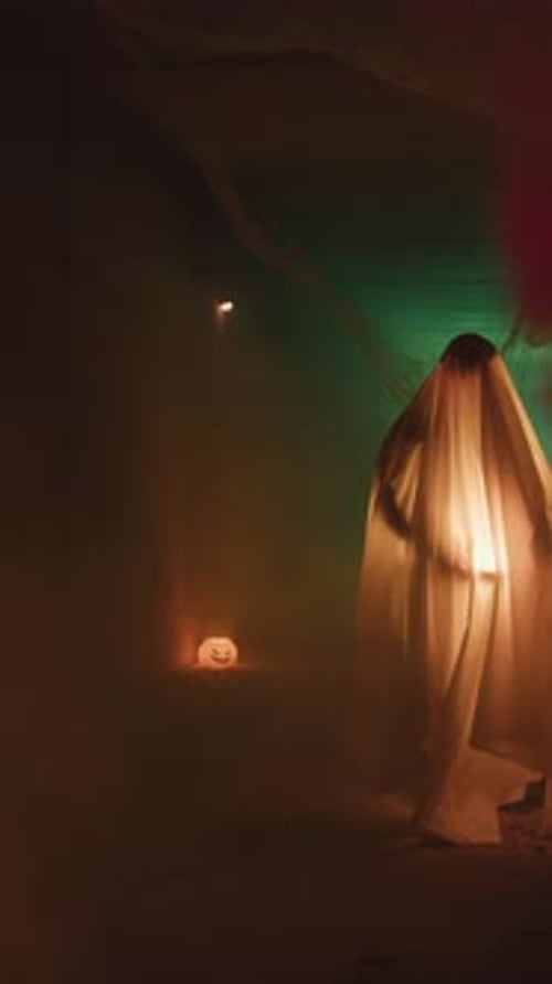 Spooky Ghost Standing by Jack-O-Lanterns in a Dark Room