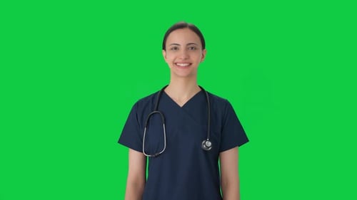 Happy Indian female doctor in scrub suit smiling Green screen
