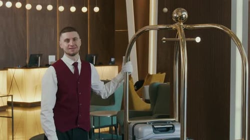 Portrait of Smiling Bellhop Standing beside Luggage Cart in Hotel Lobby