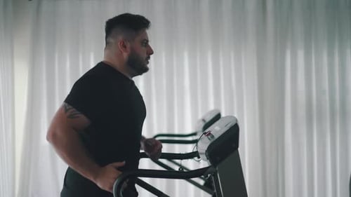 Homem forte treinando exercícios cardiovasculares na esteira na academia, visão lateral, câmera lenta