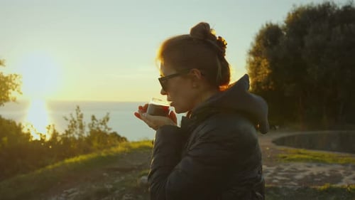 Woman Drinks Beverage on Hilltop at Sunrise