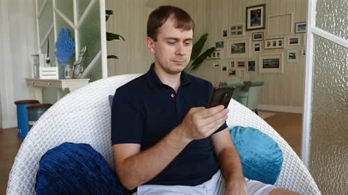 Fokussierter Mann nutzt Smartphone im modernen Wohnzimmer, Haustechnik und Entspannung
